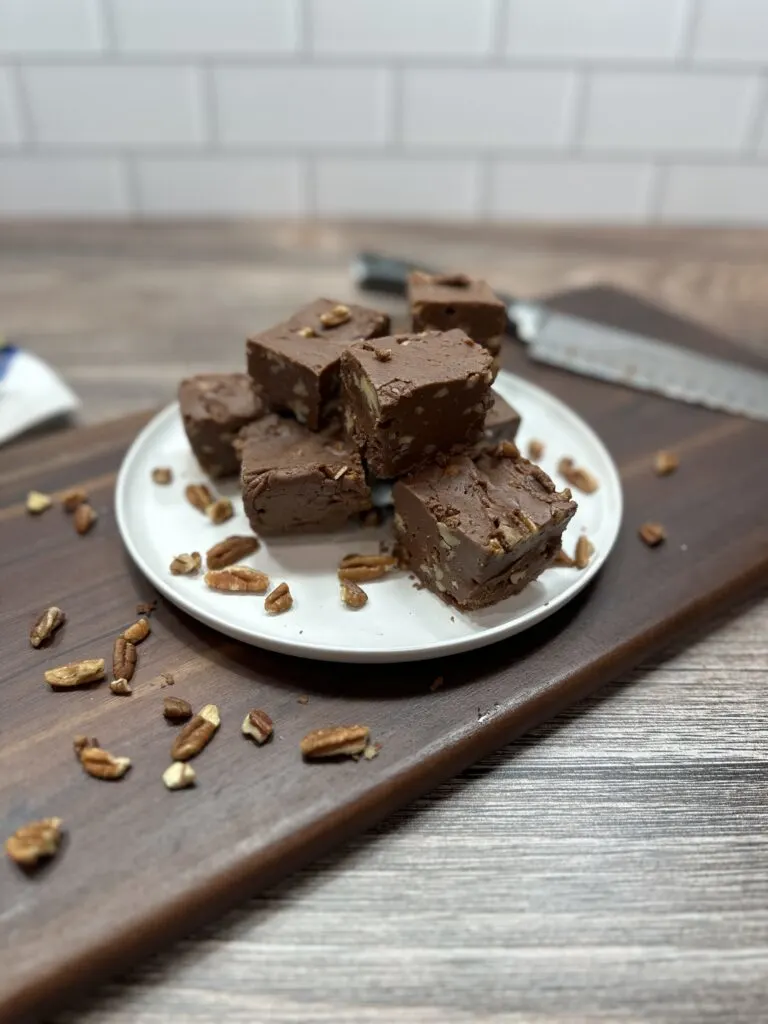 Slices of fudge stacked up on a white plate. There's a sharp knife on the cutting board.