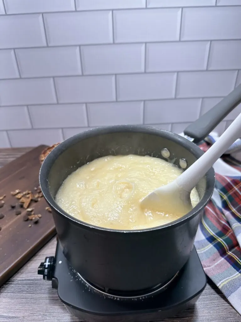 Sauce pan on a heater containing a mixture of butter, evaporated milk, and sugar stirred thoroughly.