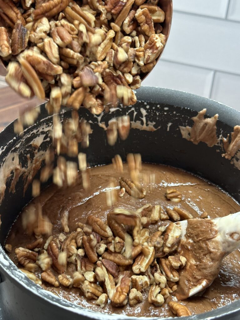 Pouring chopped pecans into a sauce pan containing the mixture of the previous ingredients.