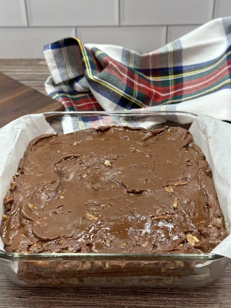 Almond fudge sitting in a glass pan after cooling off. There is a piece of parchment paper sitting in between the fudge and the glass pan.