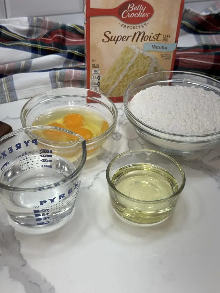 Image of vanilla cake mix, eggs, water, and vegetable oil in separate bowls ready to be mixed.