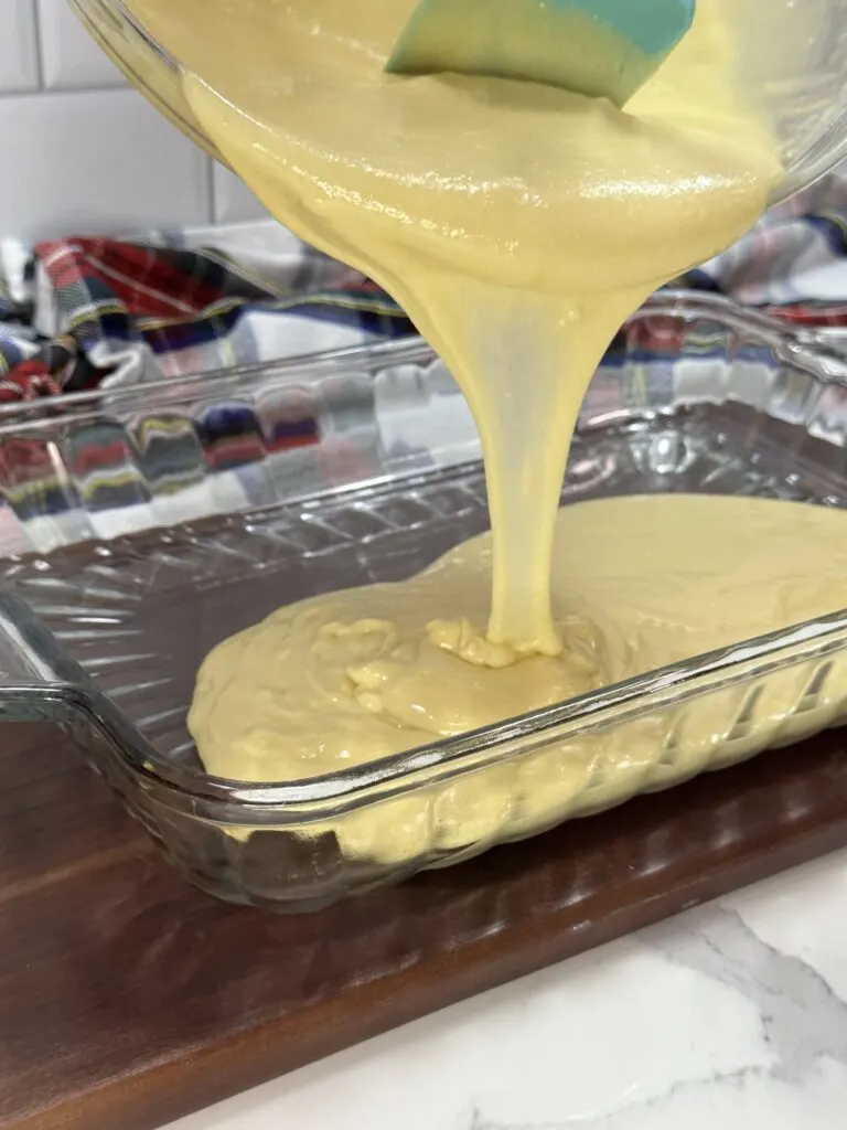 Image of required cake ingredients mixed thoroughly being poured into a glass baking dish.