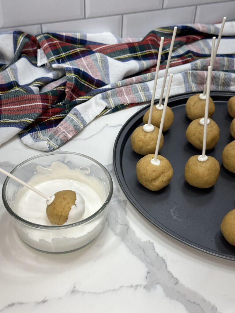 Image of cake pop being dipped into the melted candy melt. On the right there are cake pops ready to be dipped.