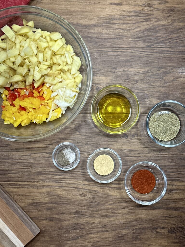 chopped potatoes, bell peppers, and onion in a bowl. near the bowl is olive oil, garlic powder, dried rosemary, smoked paprika, salt and pepper